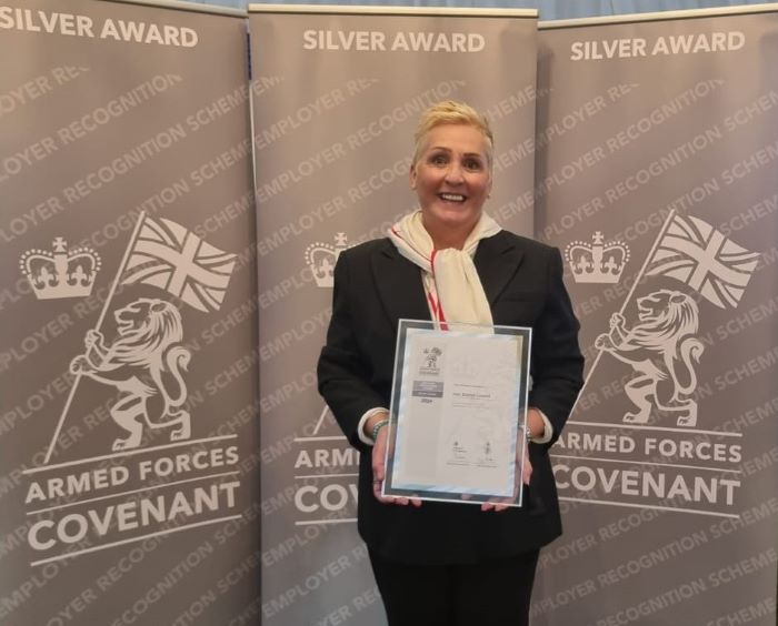 Woman holding framed certificate in front of a screen with Sllver Award printed on it and the insignia of the Armed Forces Employment Recognition Scheme