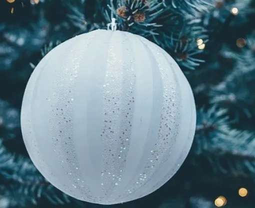 White and blue Christmas baubles on a tree with fairy lights