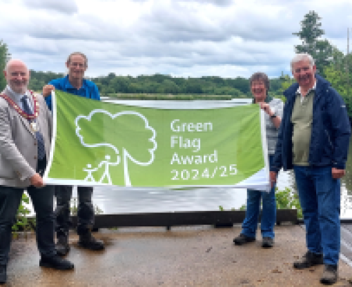 Four people holding a Green Flag in front of a lake and trees and bushes