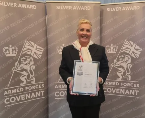 Woman holding framed certificate in front of a screen with Silver Award printed on it and the insignia of the Armed Forces Employment Recognition Scheme