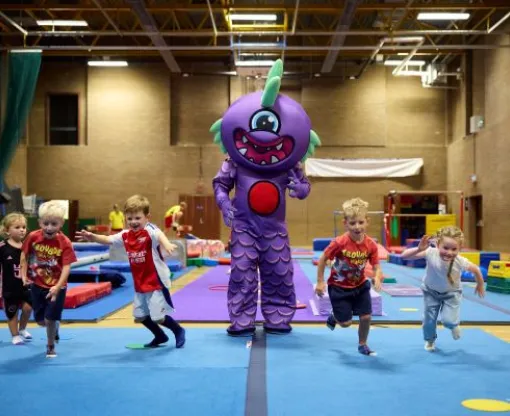 Children in a sports hall running away from a large purple cartoon style monster