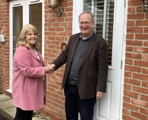 A man and a woman shaking hands outside a red brick house with a white door