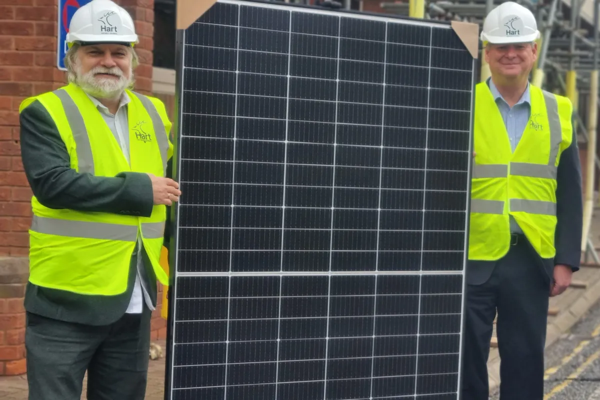 Two men in hard hats and hi viz jackets holding solar panel