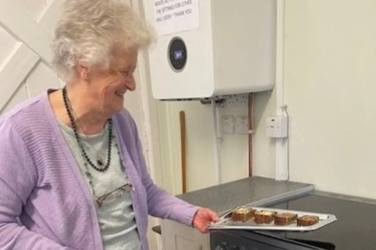 Older woman holding a tray of cakes beside a new oven