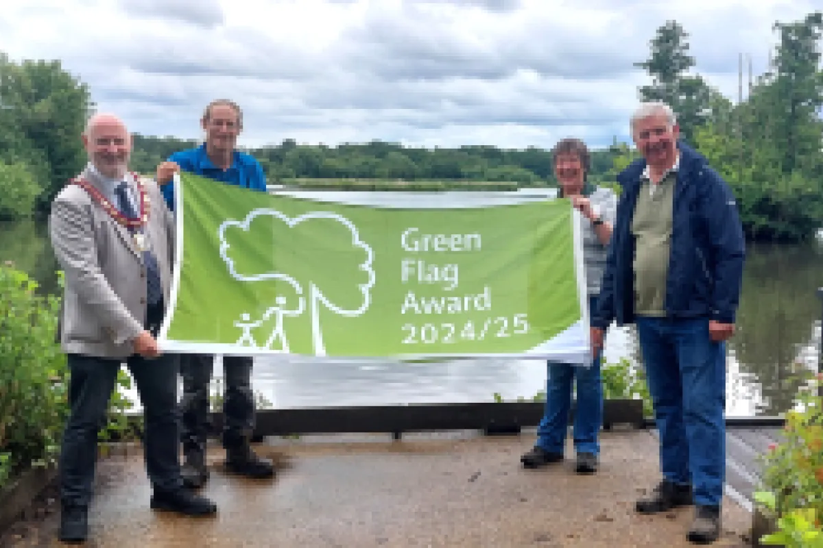 Four people holding a Green Flag in front of a lake and trees and bushes