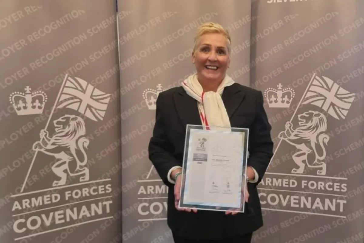 Woman holding framed certificate in front of a screen with Sllver Award printed on it and the insignia of the Armed Forces Employment Recognition Scheme