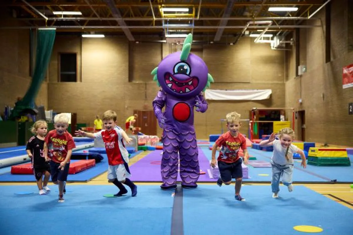 Children in a sports hall running away from a large purple cartoon style monster