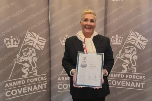 Woman holding framed certificate in front of a screen with Sllver Award printed on it and the insignia of the Armed Forces Employment Recognition Scheme