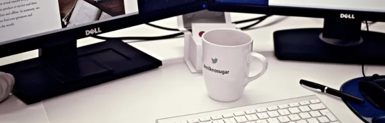 Office desk with laptop, screens and coffee cup