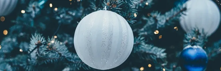 White and blue Christmas baubles on a tree with fairy lights