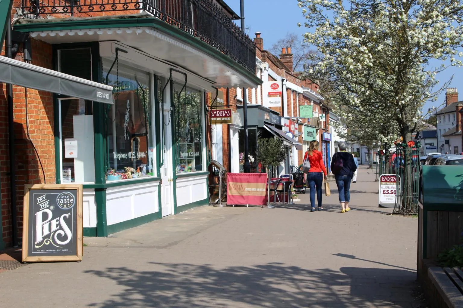 Two people walking past shops on Hartley Wintney high street