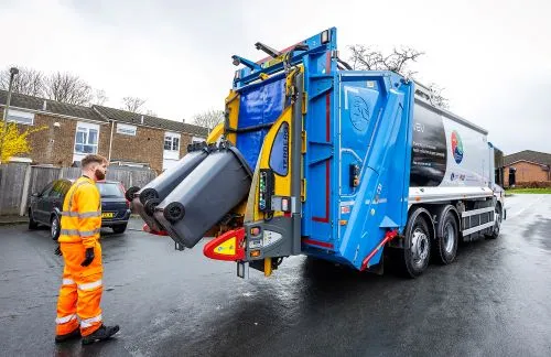 Man in an orange high viz suit collects black bins in the zero-emission bin truck