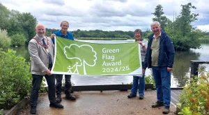 Four people holding a Green Flag in front of a lake and trees and bushes