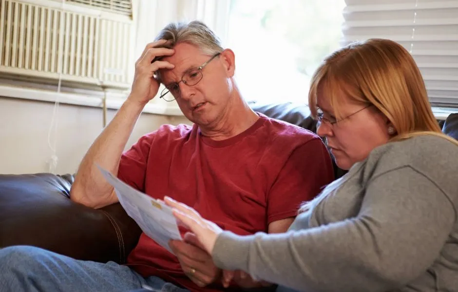 Man and woman sitting on sofa looking worried with a bill in the woman's hand